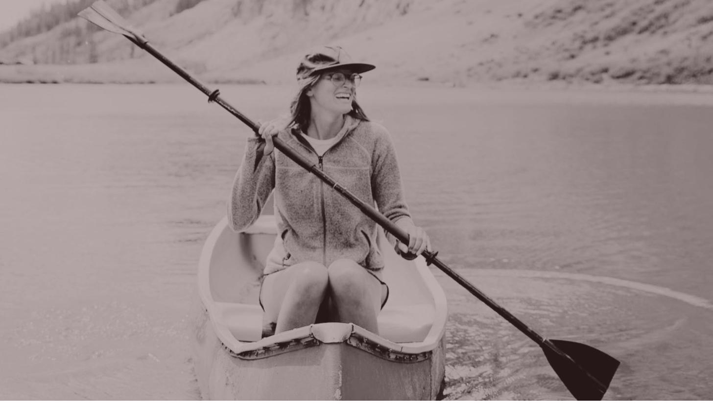Rita laughing while paddling a canoe on a calm mountain lake
