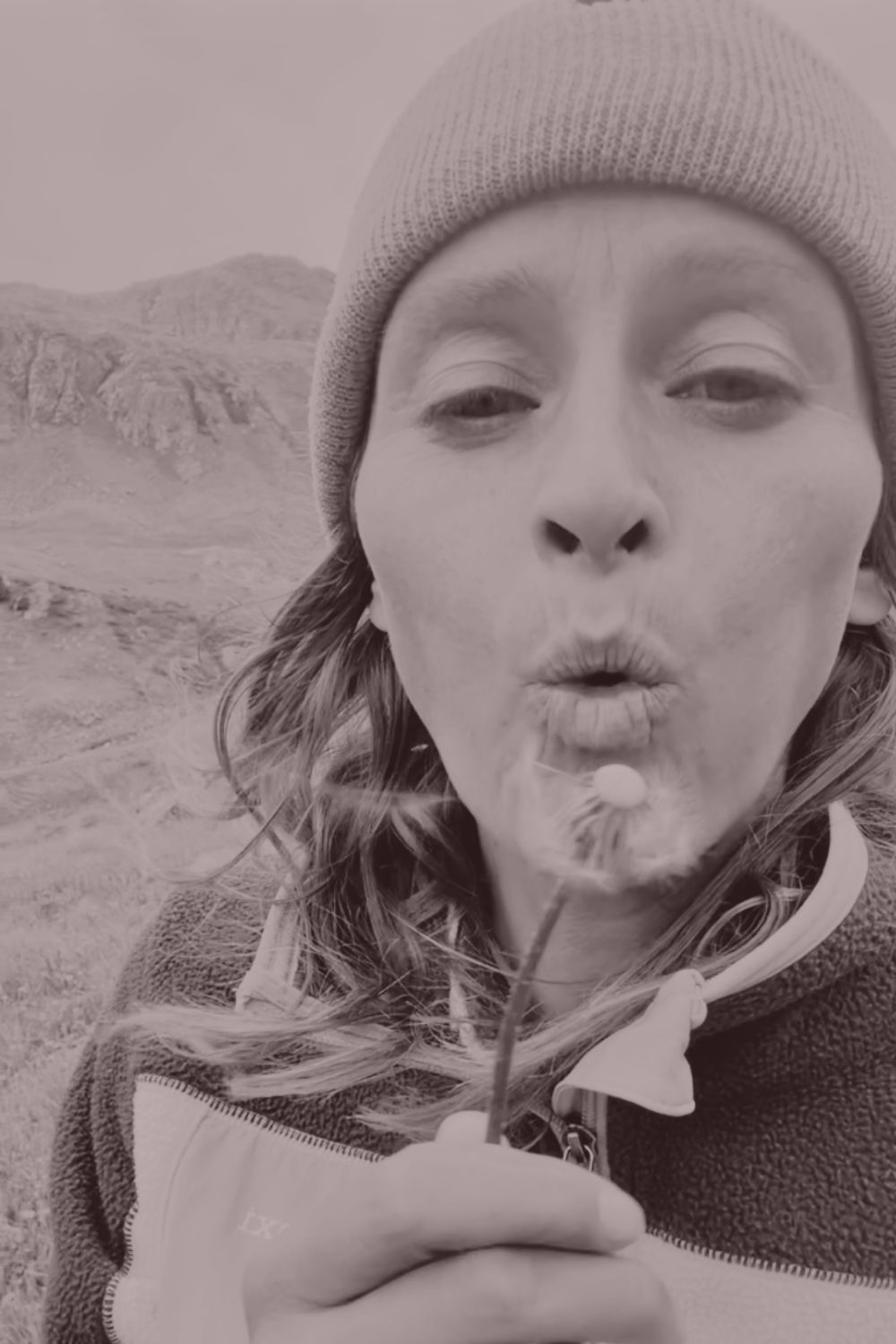 A woman blowing the seeds off a dandelion into the mountain wind