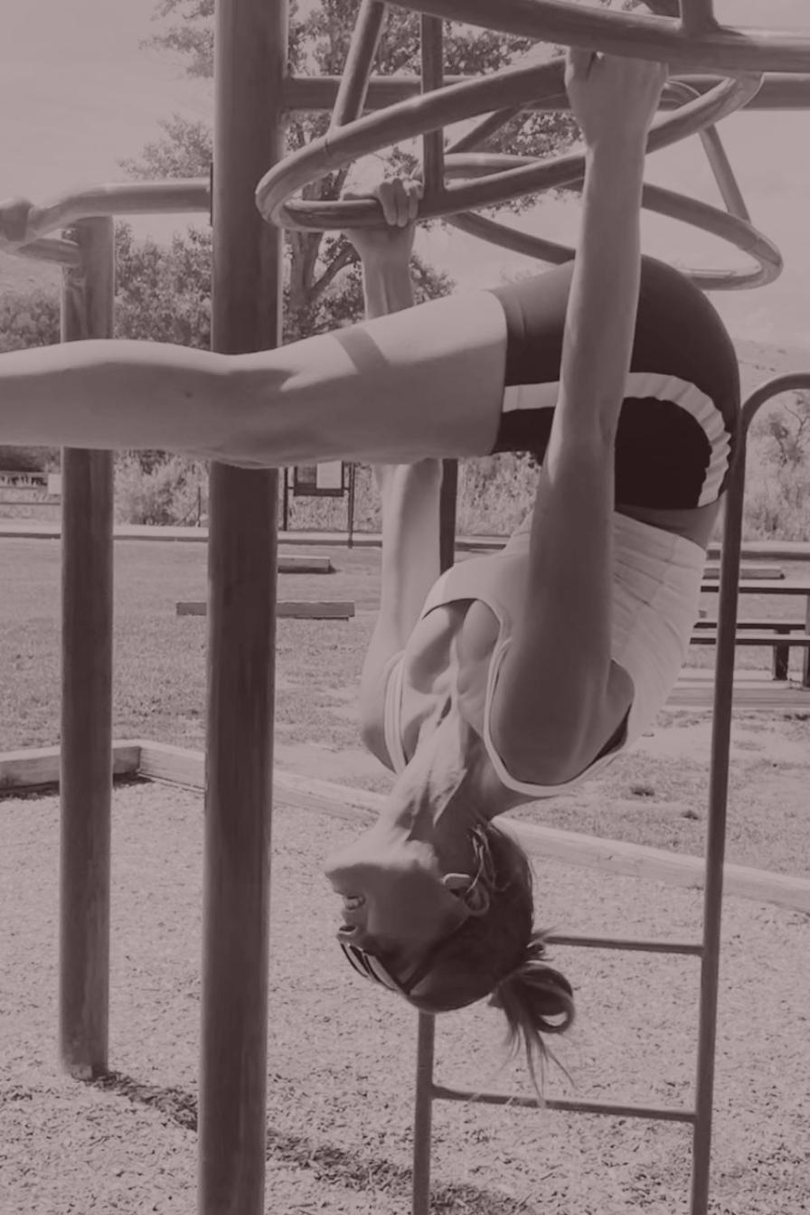 A woman hanging upside down from playground monkey bars, laughing