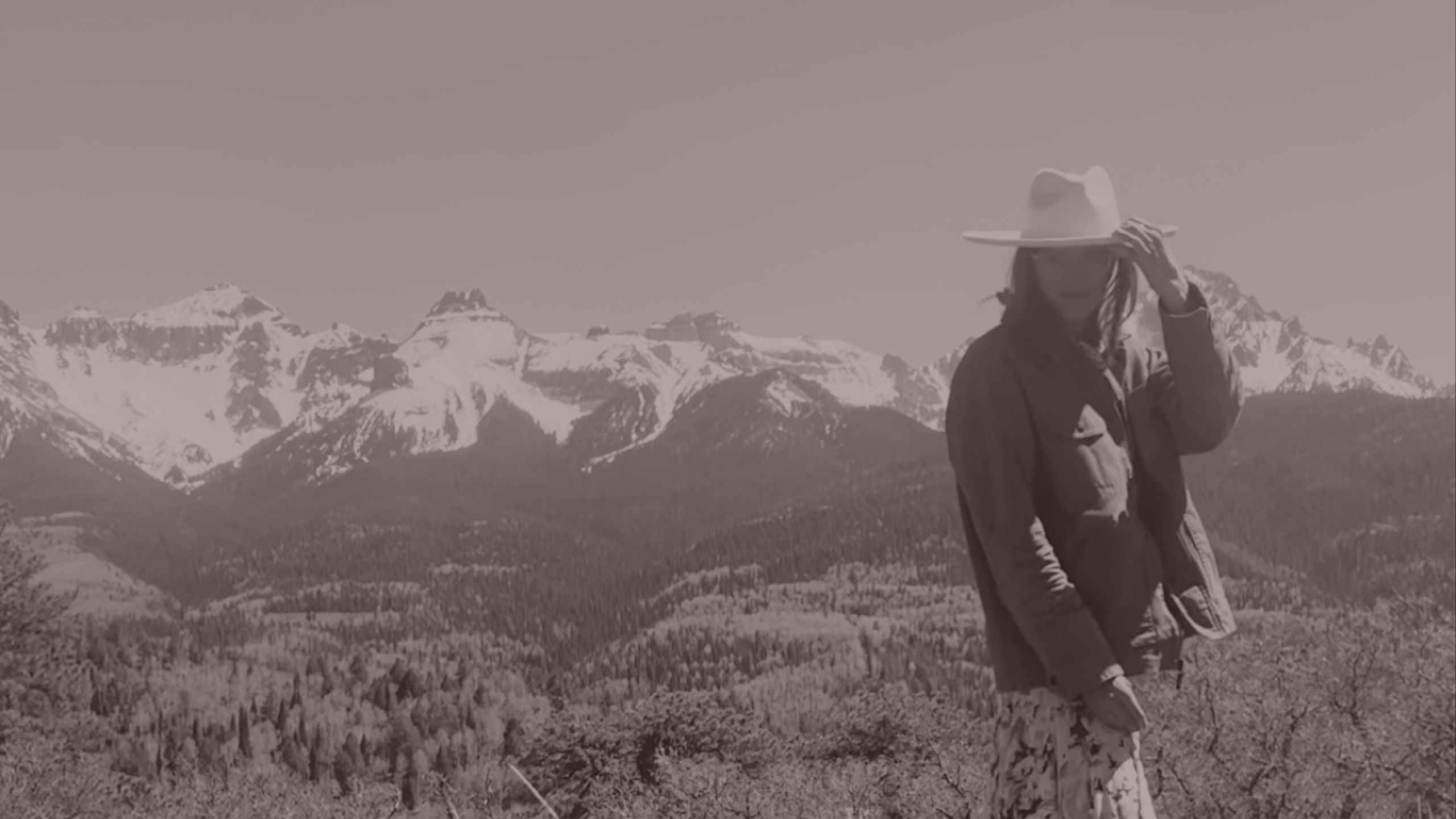 A woman looking out over open mountains, wearing a wide-brimmed hat