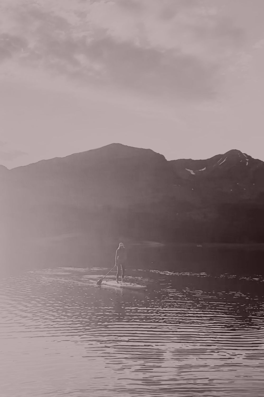 A woman paddleboarding on a still mountain lake at dawn