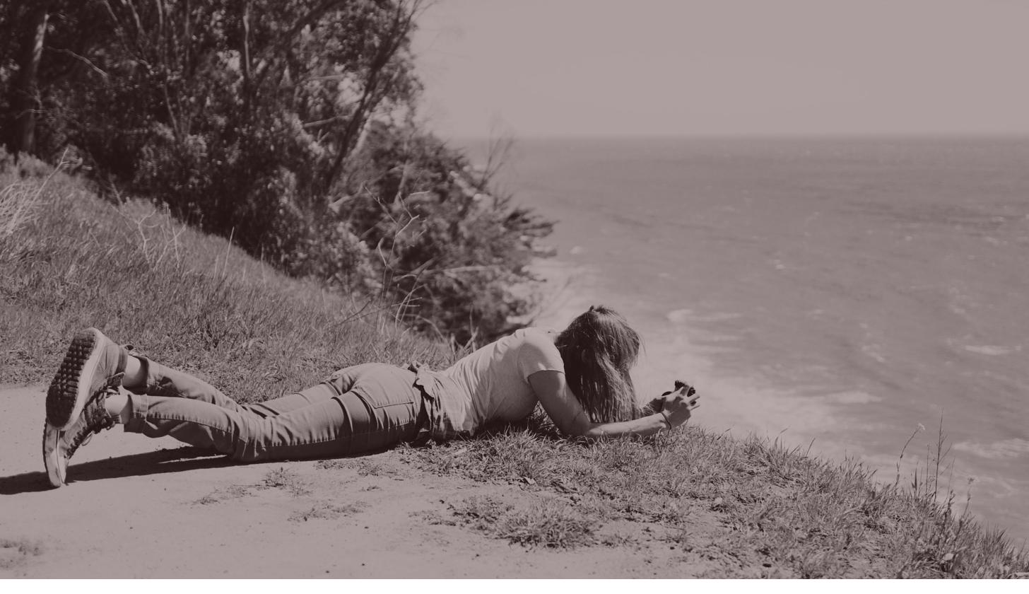 Rita lying at the edge of a cliff, fully absorbed in capturing a photograph