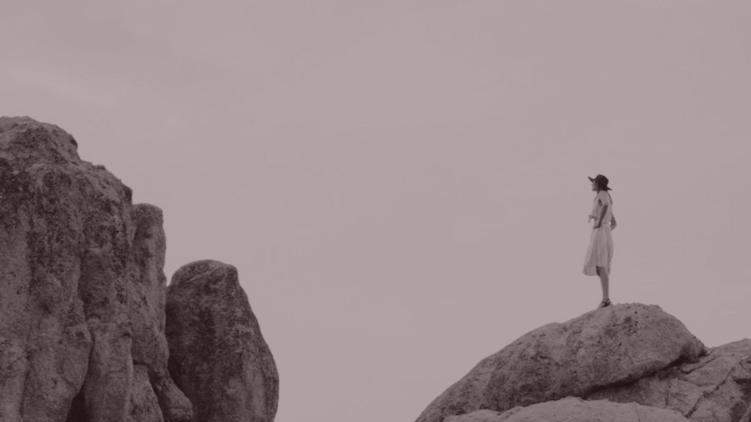 A woman standing on a rock formation, overlooking open landscape
