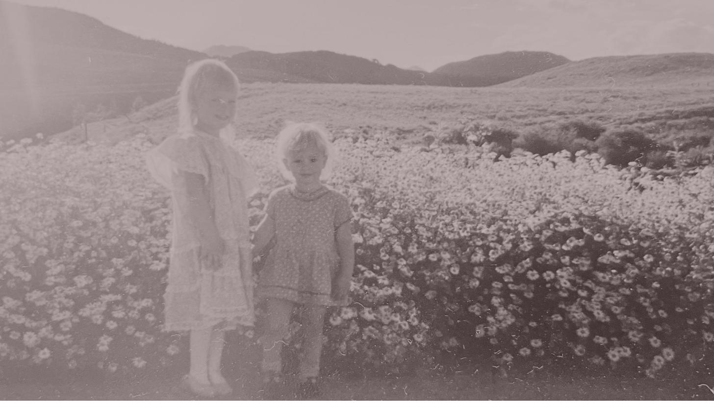 Two sisters standing hand in hand in a field of wildflowers